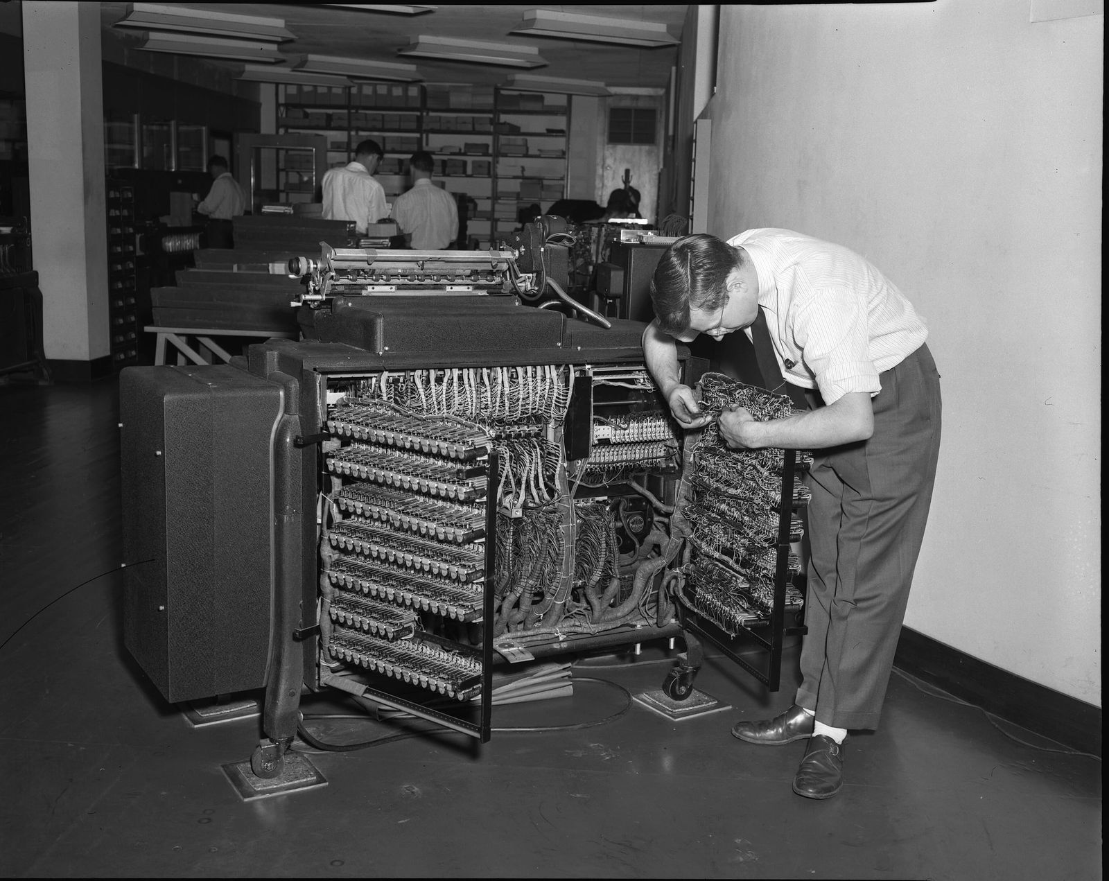 Técnico revisando el cableado interno de una tabuladora en una sala de máquinas, 1947